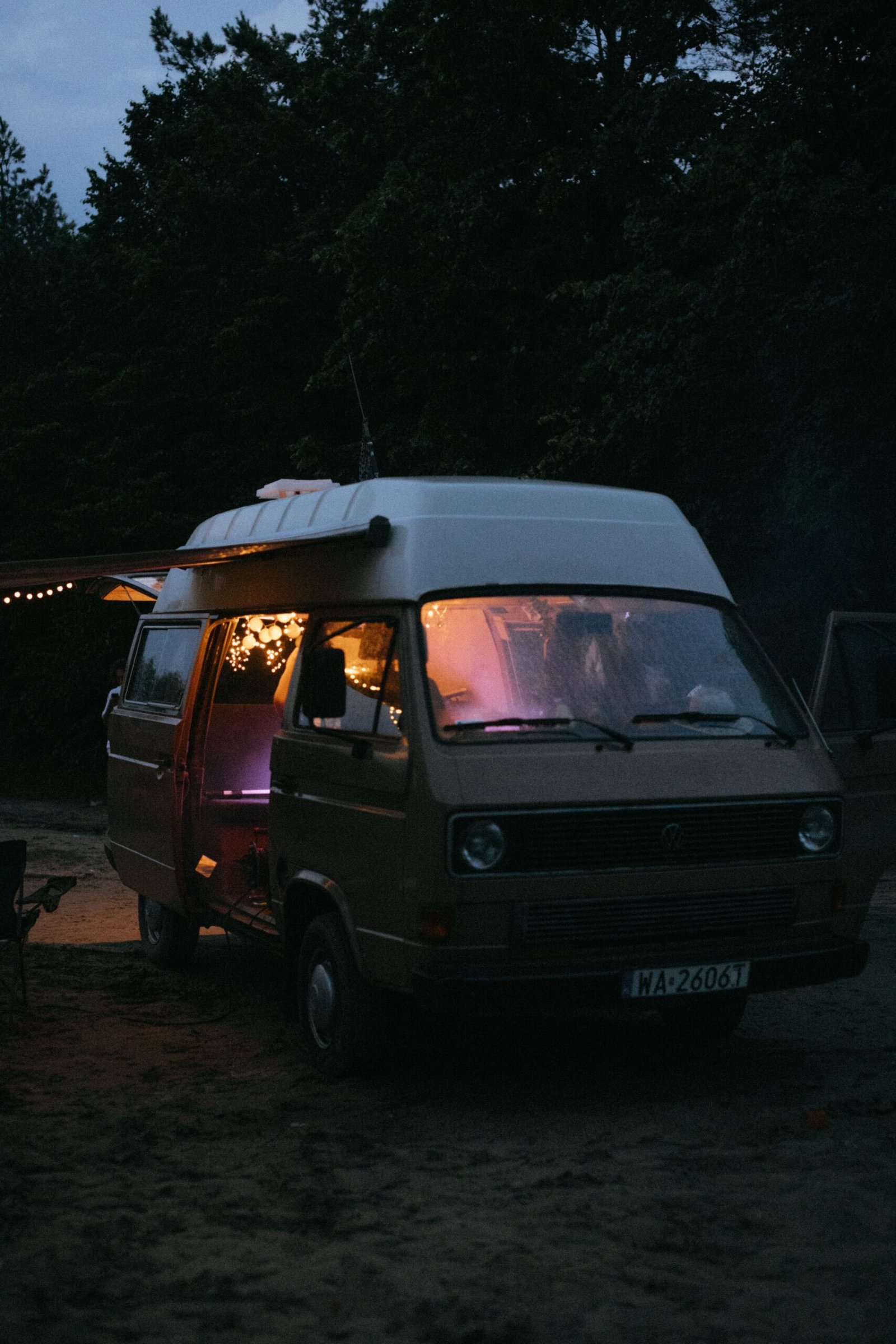 Camper iluminada con luz cálida en un bosque al anochecer