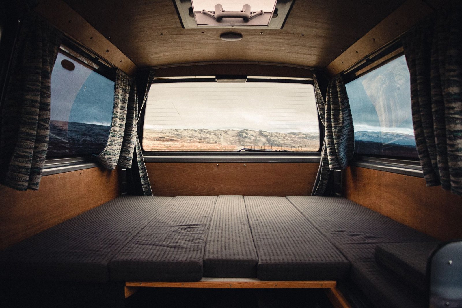 Interior de camper terminado con cama, grandes ventanas y paisaje exterior