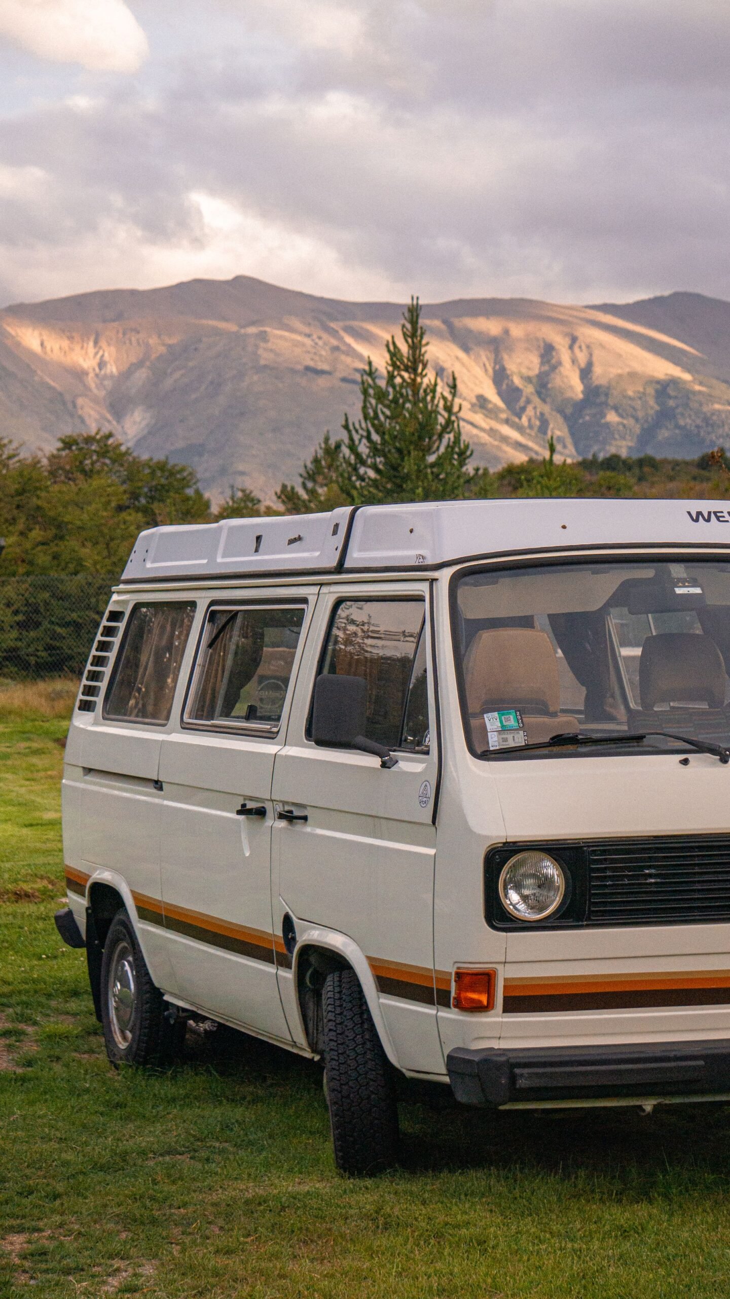 Camper clásica en un campo con montañas y luz de atardecer
