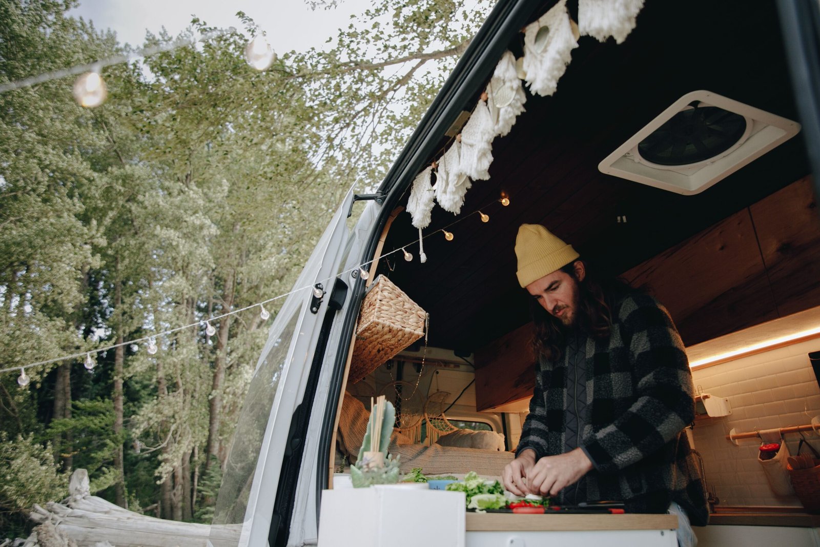 Persona preparando comida en una camper abierta hacia un bosque