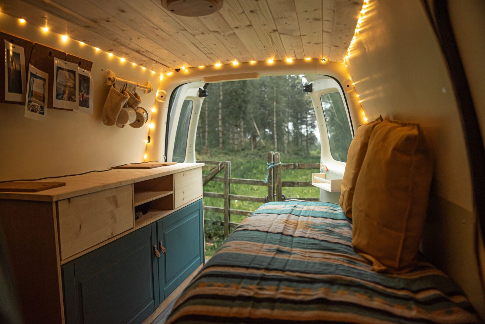 Interior de camper acogedor con madera, cama, luces cálidas y vistas al bosque