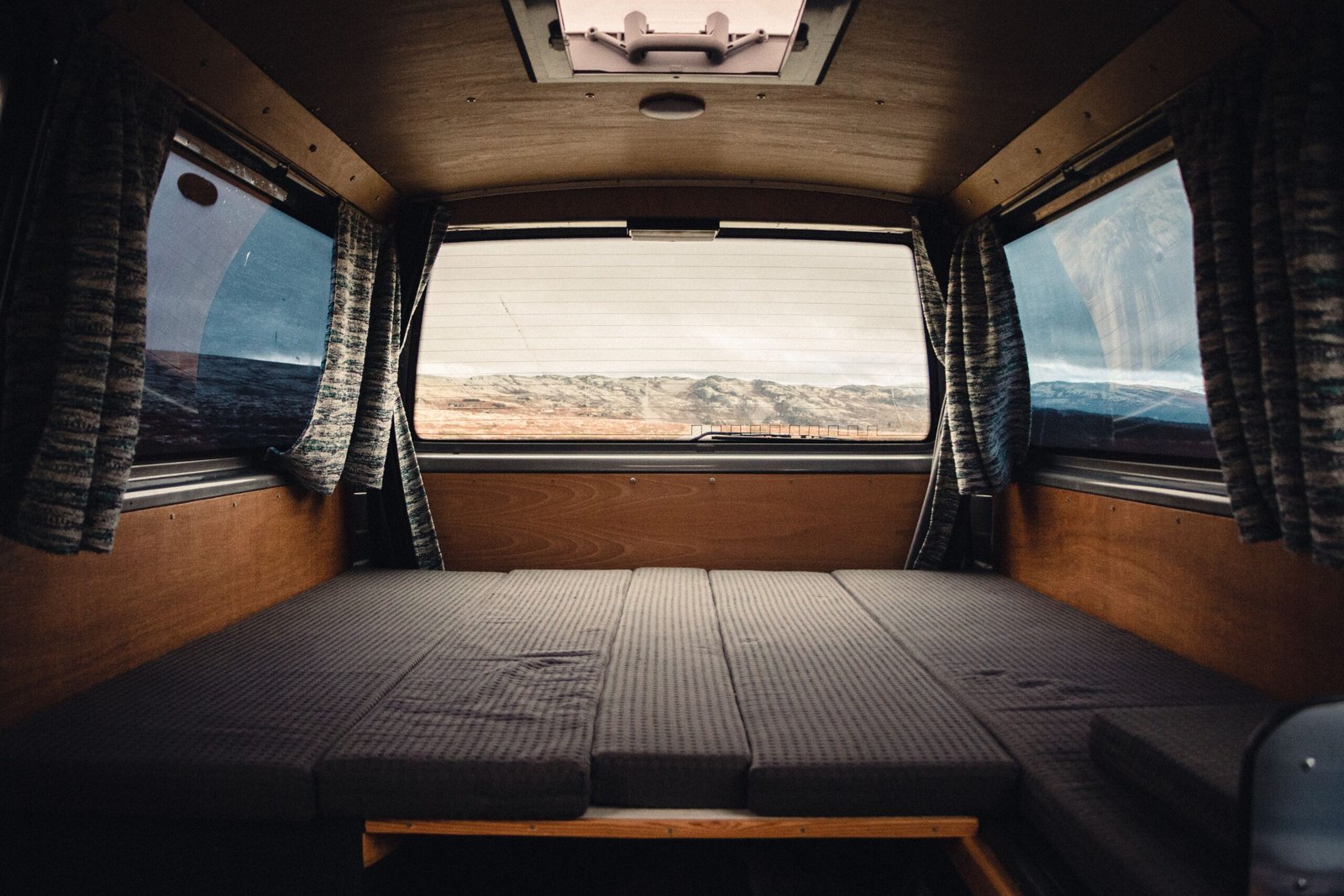 Cama interior de camper con grandes ventanas hacia un paisaje natural