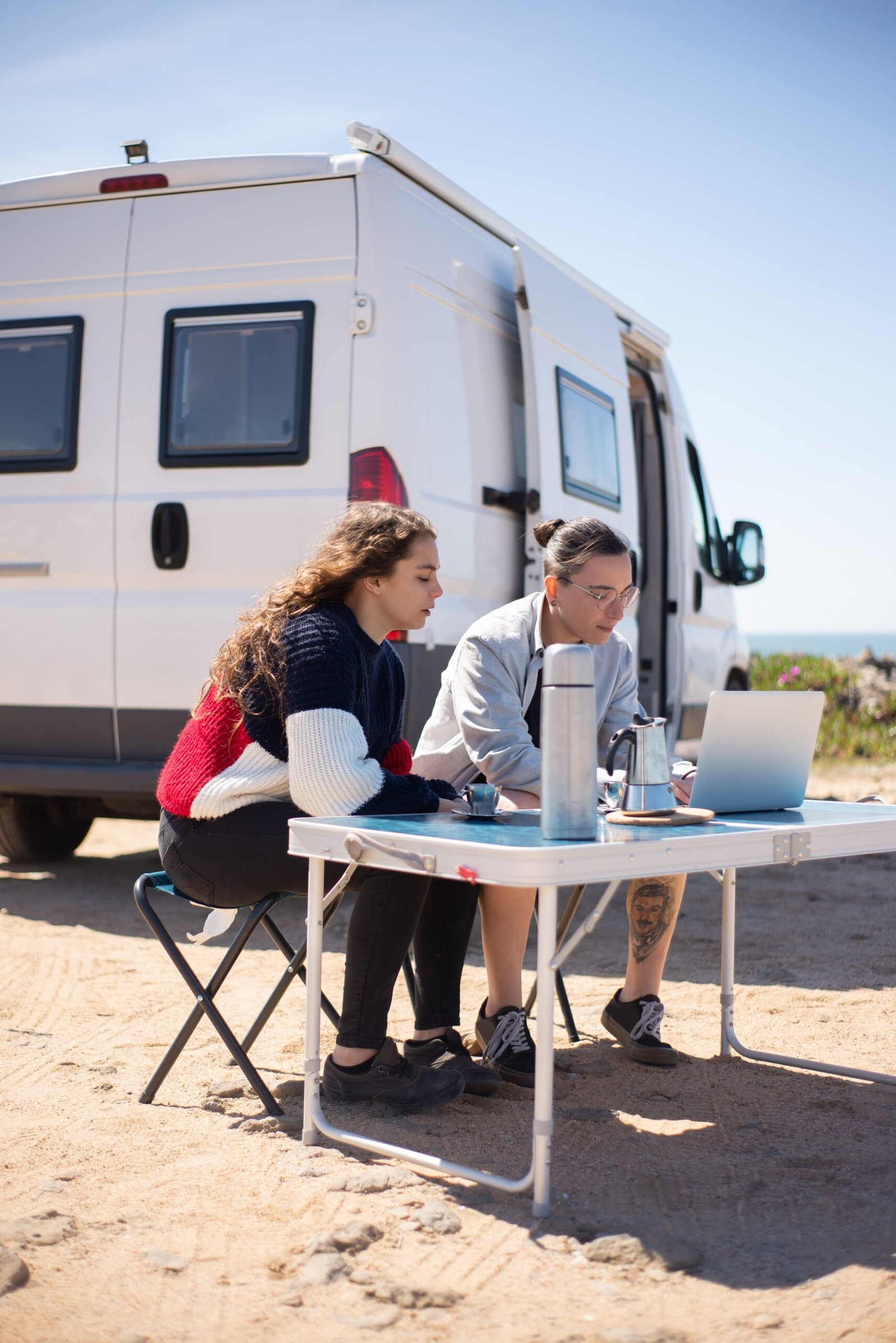 Dos personas planificando un viaje junto a una camper con un portátil