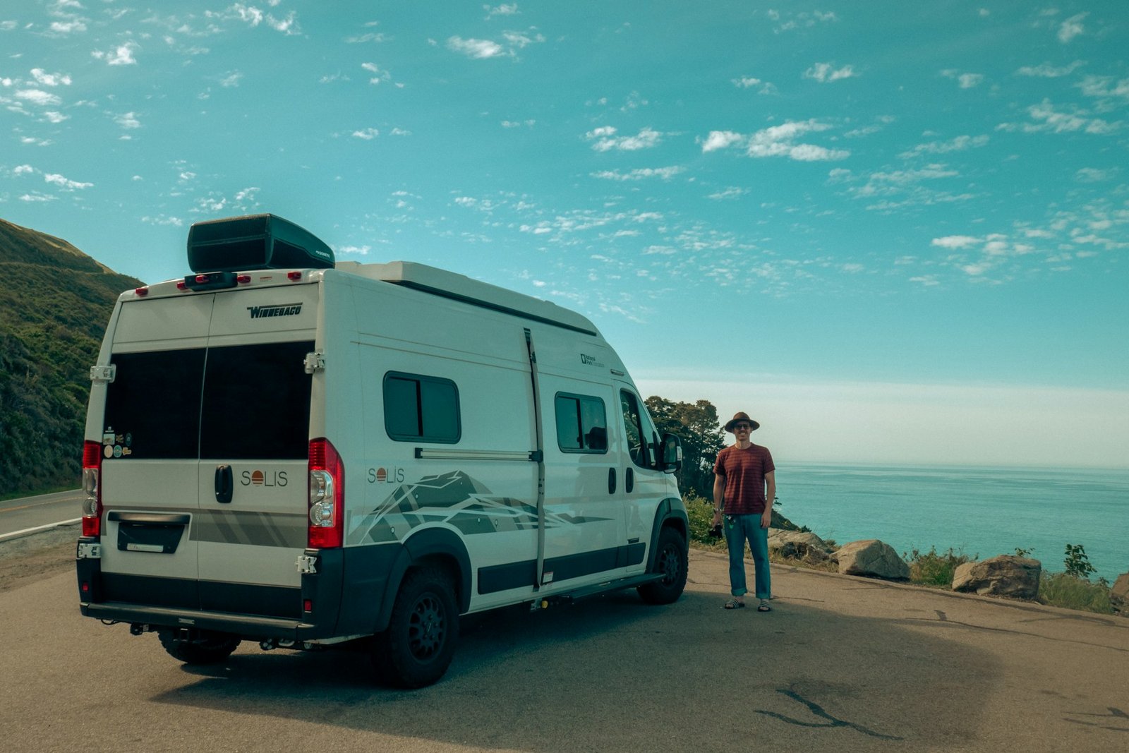 Viajero junto a la camper en la costa, escena editorial de ambiente para la guía Dethleffs