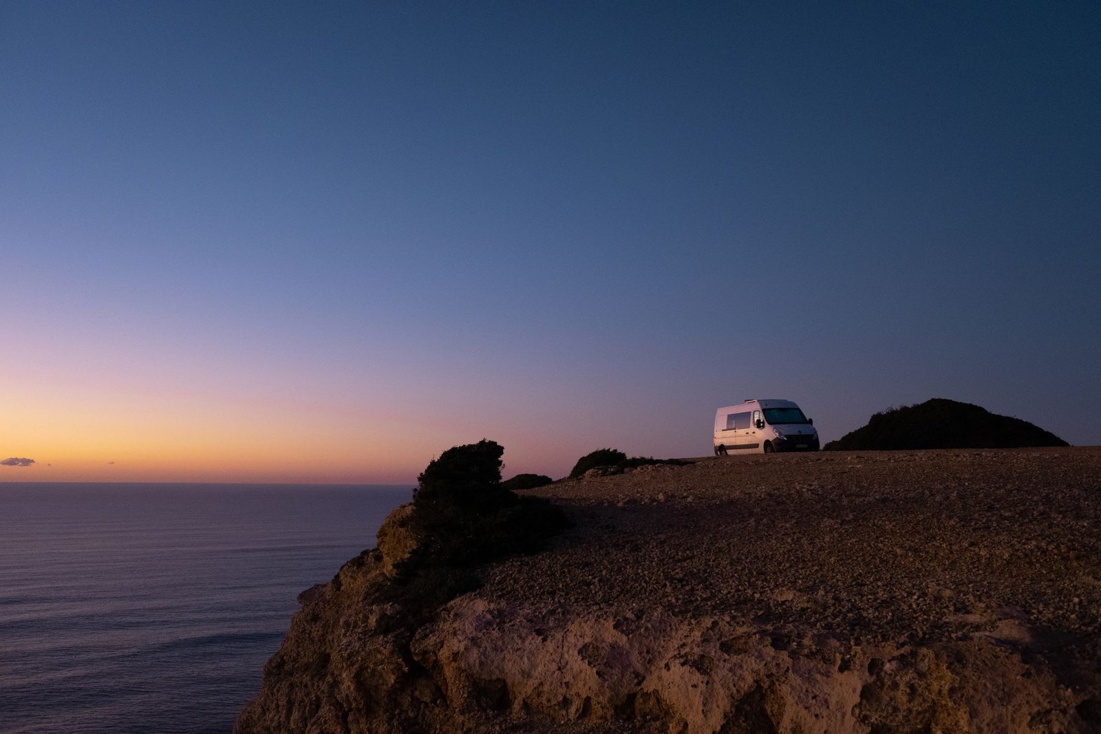 Furgoneta camper frente al océano desde un acantilado al atardecer