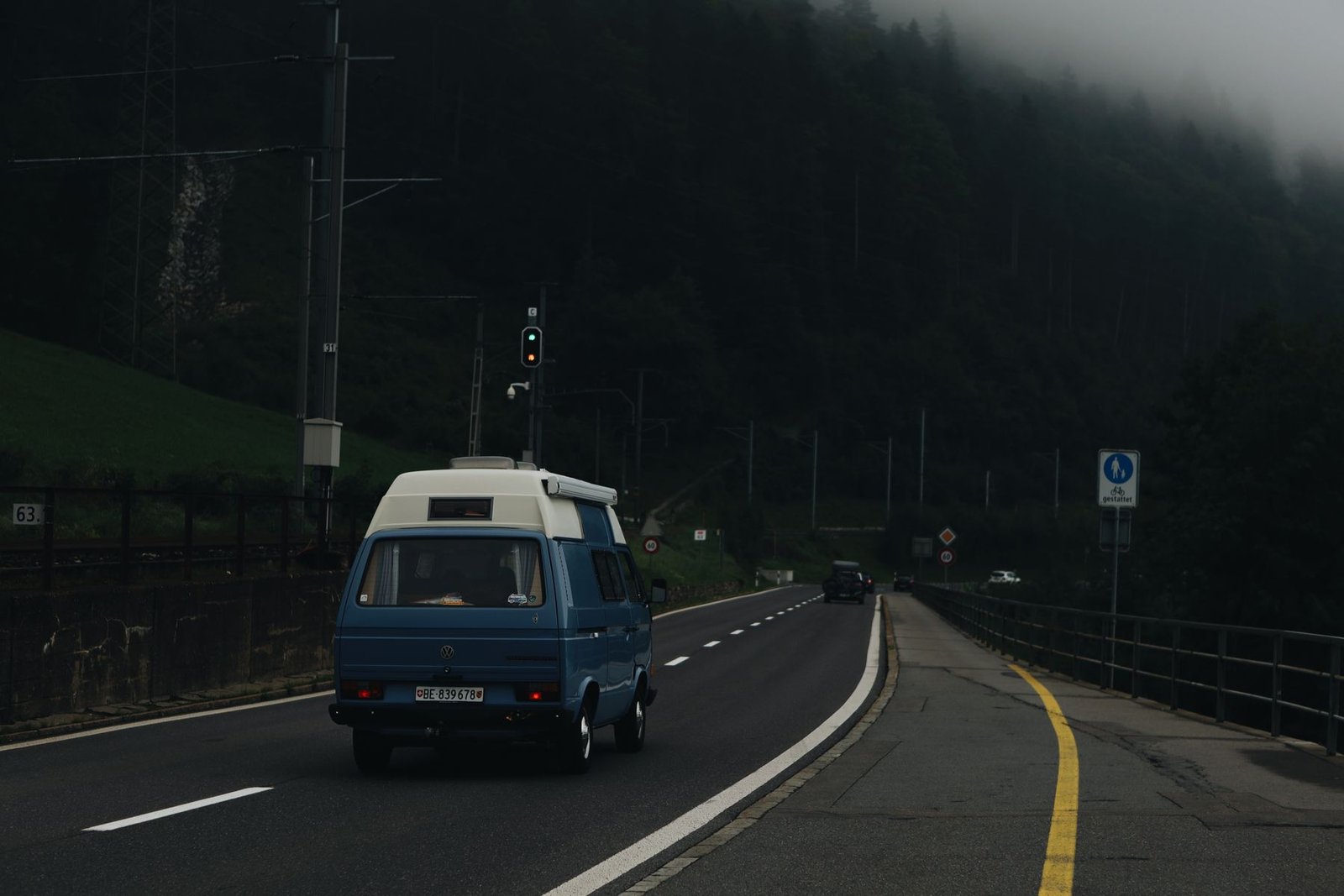 Furgoneta Volkswagen camper azul en una carretera entre montañas y bosque con niebla